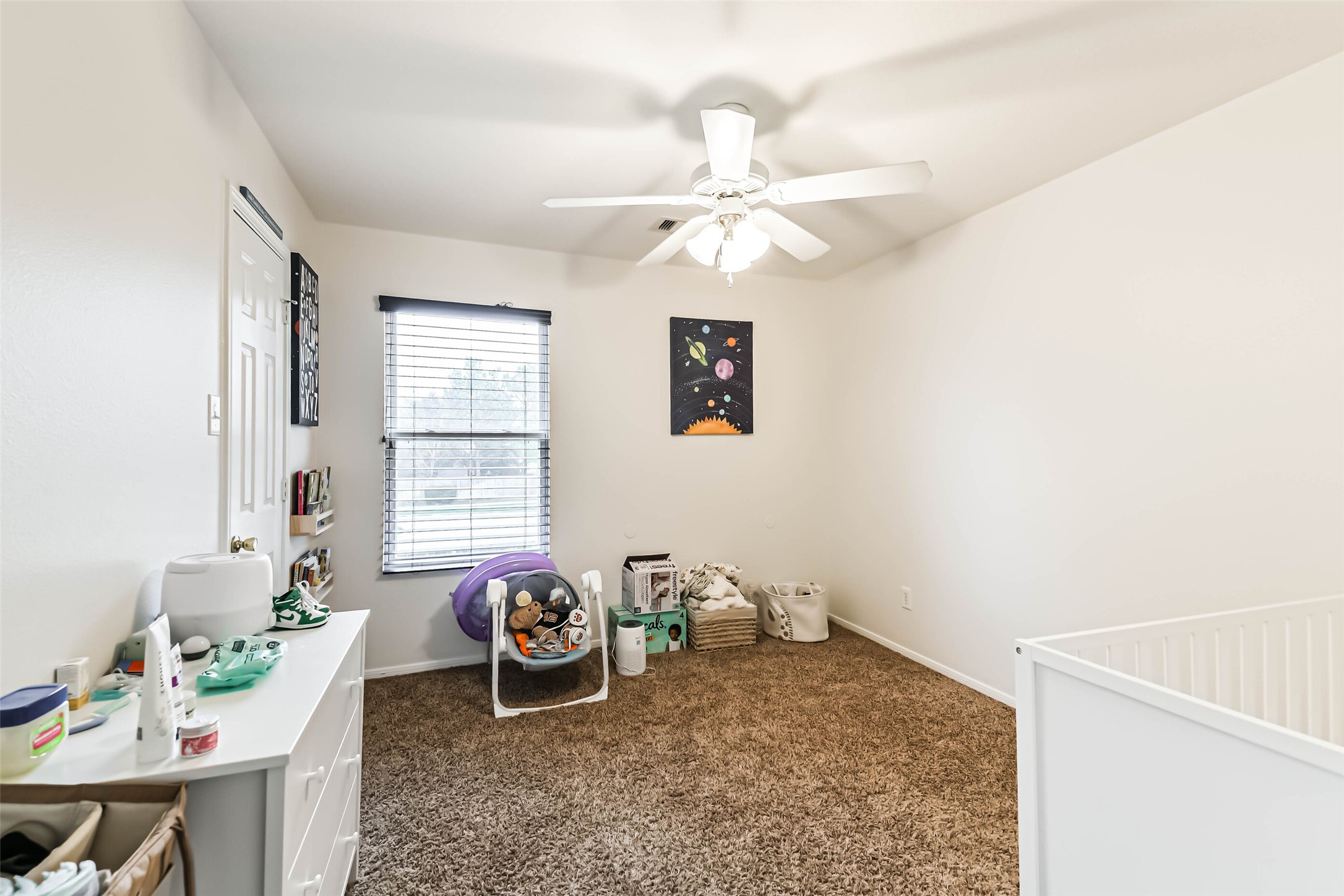 22538 Goss Spring Court Spring, TX 77373 - Photo 28 of 36 Bright and cozy bedroom with neutral walls and carpet, featuring a ceiling fan and a window for natural light. The room includes a small dresser, crib, and playful decor, making it ideal for a child's space.