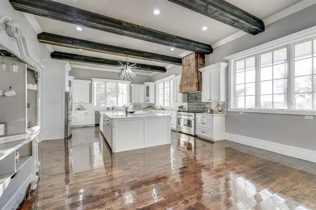 a large white kitchen with granite countertop a stove a sink and white cabinets with wooden floor