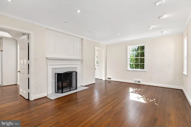 a view of an empty room with wooden floor fireplace and a window