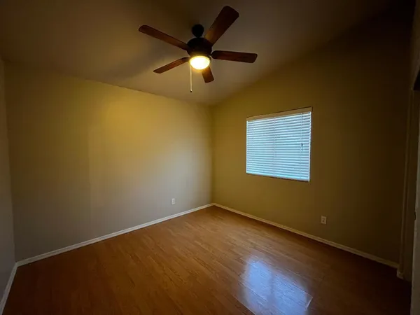 a view of an empty room with wooden floor and a ceiling fan
