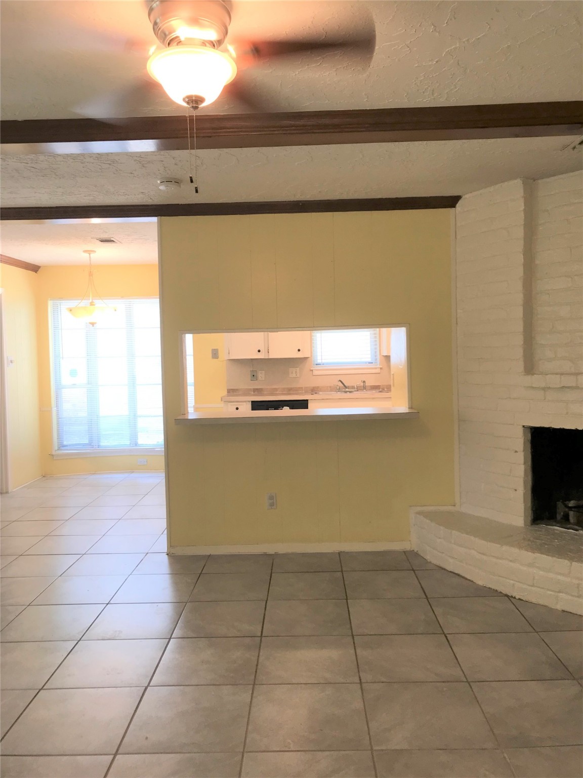 12331 Scarcella Lane Meadows Place, TX 77477 - Photo 6 of 13 This room features a spacious open layout with a cozy brick fireplace. A ceiling fan provides comfort, and a serving hatch connects to the kitchen, allowing for easy meal service.