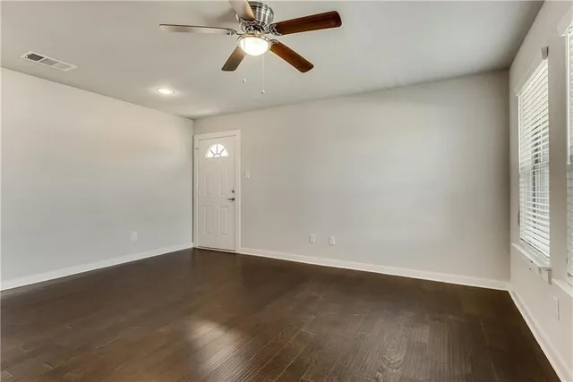 an empty room with wooden floor fan and windows