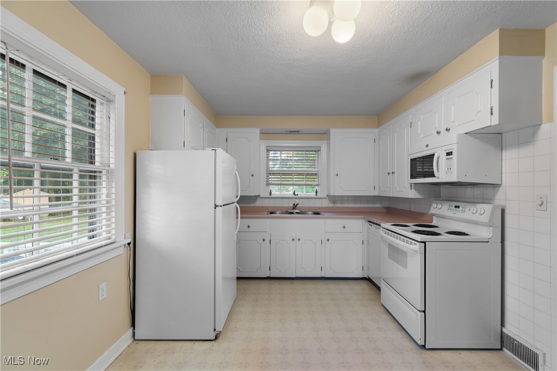 955 Raff Road Southwest Canton, OH 44710 - Photo 9 of 33 Kitchen with white appliances, light flooring, a textured ceiling, white cabinetry, and backsplash