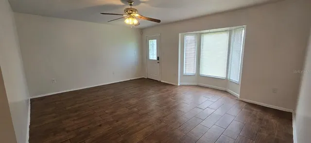 an empty room with wooden floor chandelier fan and windows