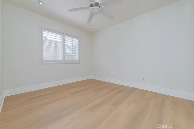 a view of an empty room with wooden floor and a ceiling fan