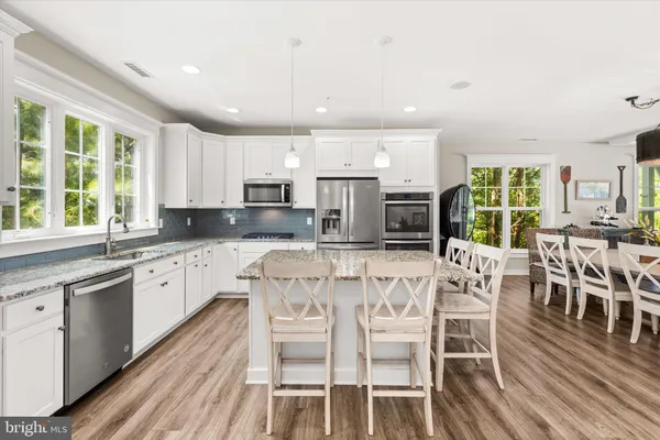 a kitchen with stainless steel appliances granite countertop a stove top oven a sink dishwasher a dining table and chairs with wooden floor