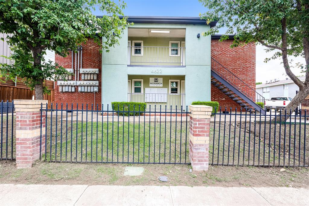 4622 Monarch Street, Unit 202 Dallas, TX 75204 - Photo 1 of 16 Two-story building featuring a brick facade with a light green stucco accent, black metal exterior staircase, ground-level entry, and a black wrought iron fence with brick pillars