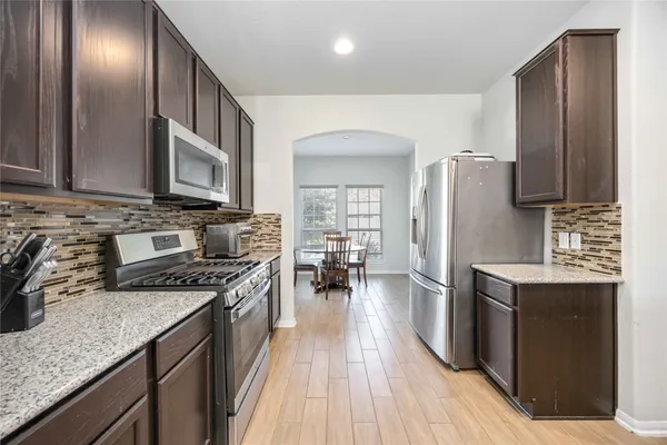 a kitchen with granite countertop stainless steel appliances a stove top oven a sink dishwasher a refrigerator and cabinets with wooden floor