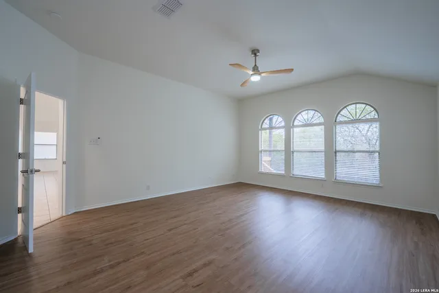 an empty room with wooden floor chandelier fan and windows