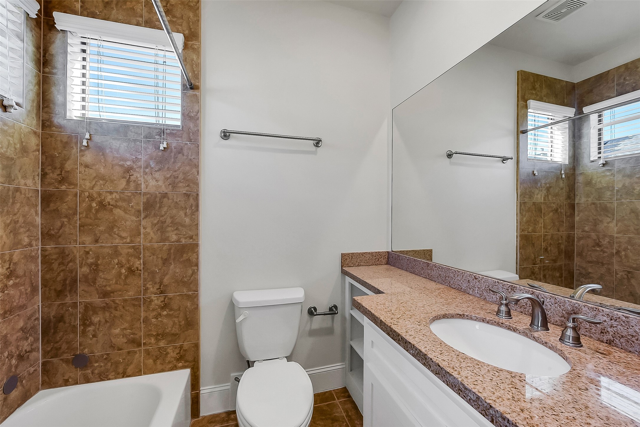 1929 Summer Street Houston, TX 77007 - Photo 19 of 27 Private en suite bath for secondary bedroom #1 on first floor features a granite vanity with storage, two privacy windows, and a tub/shower combination with tile wall.