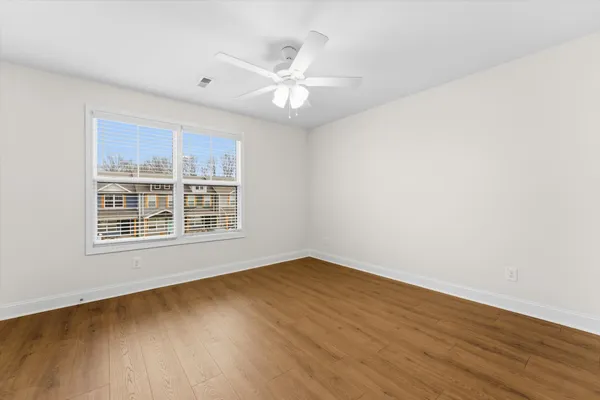 an empty room with wooden floor fan and windows