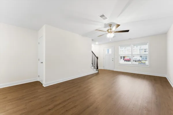 an empty room with wooden floor chandelier fan and windows