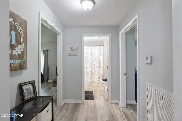 a view of a hallway to a room with wooden floor and a mirror