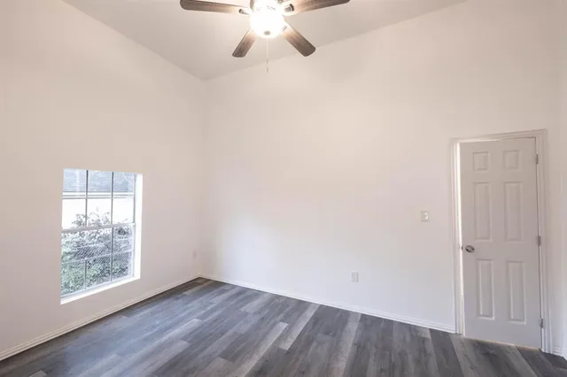 an empty room with wooden floor chandelier fan and windows