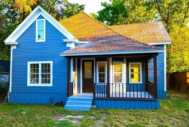 a view of brick house with a small yard plants and large tree