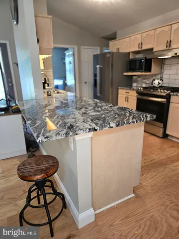 a kitchen with stainless steel appliances granite countertop a stove a refrigerator a sink a dining table and chairs