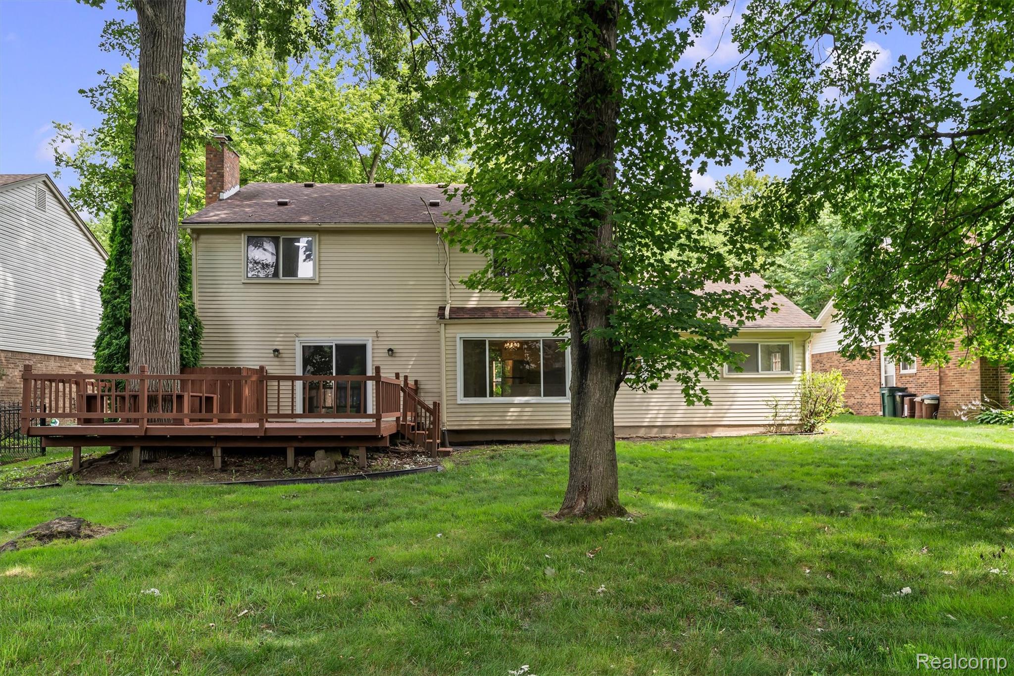 2118 Rutgers Drive Troy, MI 48085 - Photo 37 of 39 Rear exterior featuring a spacious wood-finish deck with railings, tan siding, multiple windows, and a sliding glass door