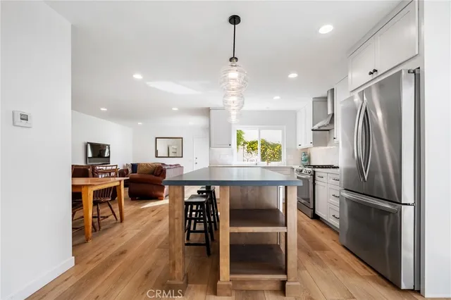 a kitchen with stainless steel appliances granite countertop a refrigerator a oven a sink a dining table and chairs with wooden floor