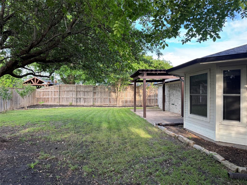6241 Peach Tree Drive Midlothian, TX 76065 - Photo 18 of 19 Expansive backyard featuring a lush lawn, mature trees, wood fence, covered patio structure, and light brick exterior
