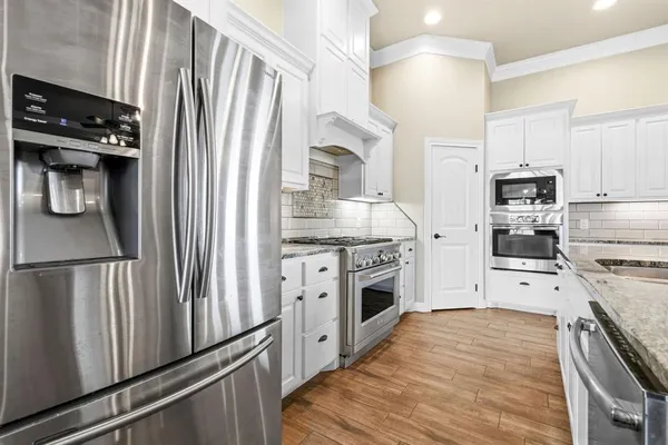 a kitchen with stainless steel appliances kitchen island granite countertop a stove top oven a sink a dining table and chairs with wooden floor