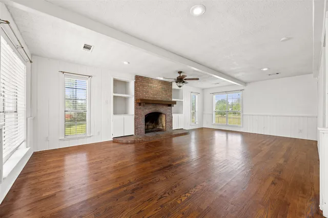 an empty room with wooden floor fireplace and windows