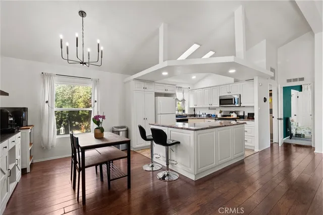 a kitchen with stainless steel appliances kitchen island granite countertop a stove a refrigerator a kitchen island a dining table and chairs with wooden floor