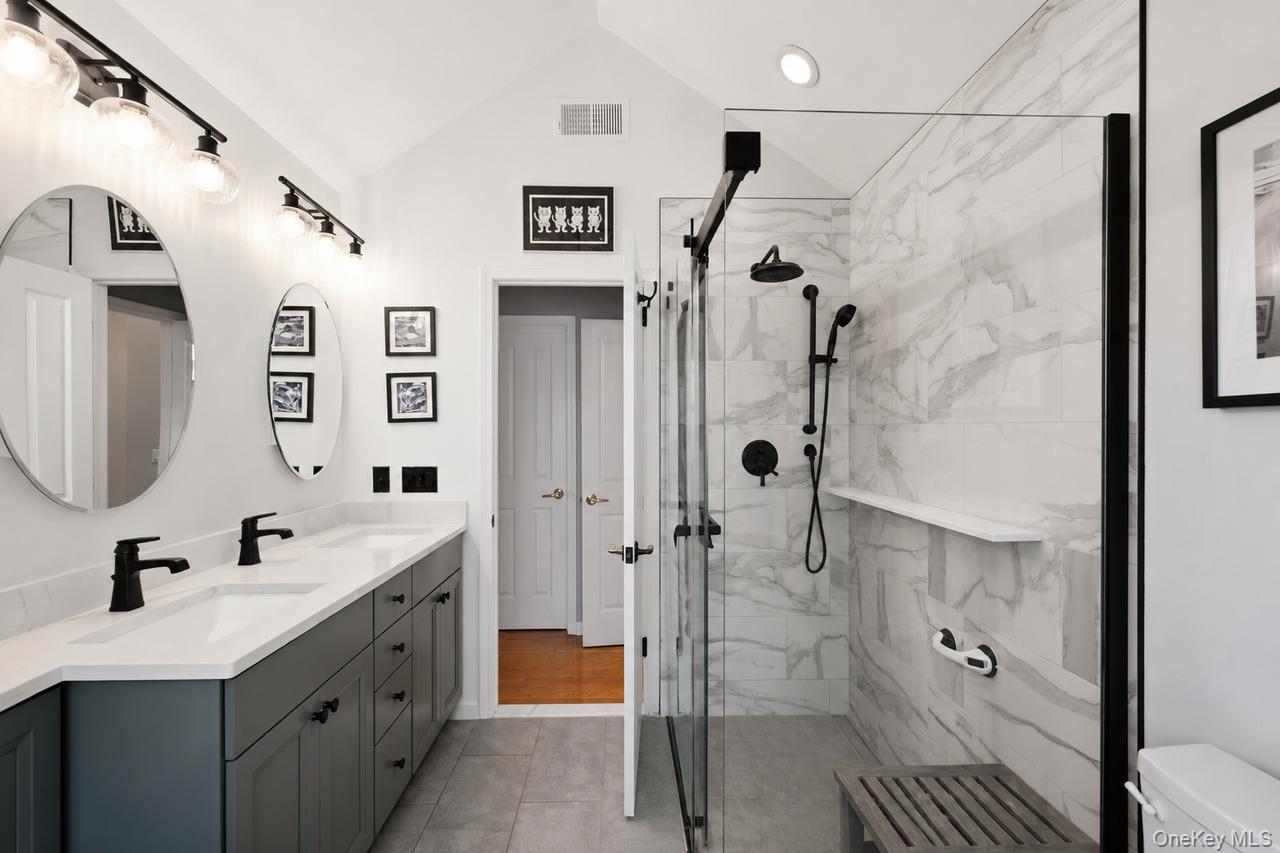 64 Roma Orchard Road Peekskill, NY 10566 - Photo 28 of 40 Vaulted ceiling bathroom featuring a dual vanity with quartz countertops, matte black plumbing fixtures, and a glass-enclosed shower with tile surround