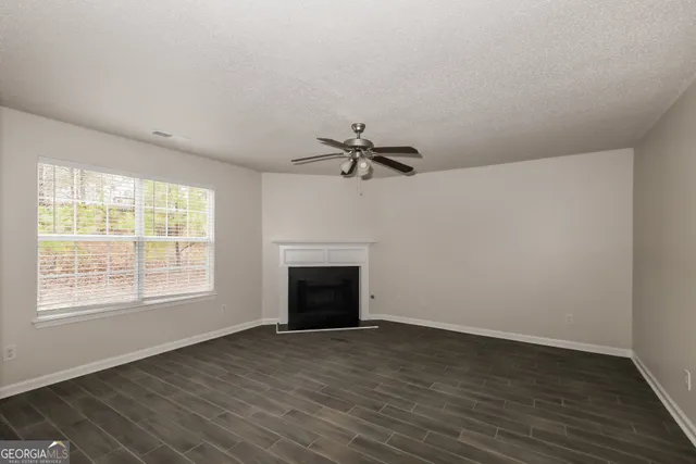 an empty room with wooden floor a ceiling fan and windows