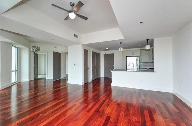 a view of an empty room with wooden floor and a ceiling fan