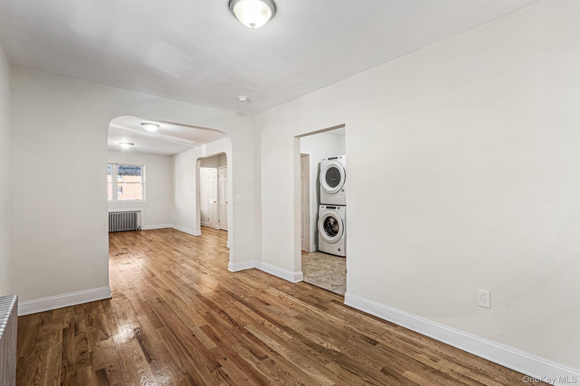 61-12 Main Street Queens, NY 11367 - Photo 17 of 35 Spare room with wood finished floors, arched walkways, stacked washing machine and dryer, and radiator heating unit