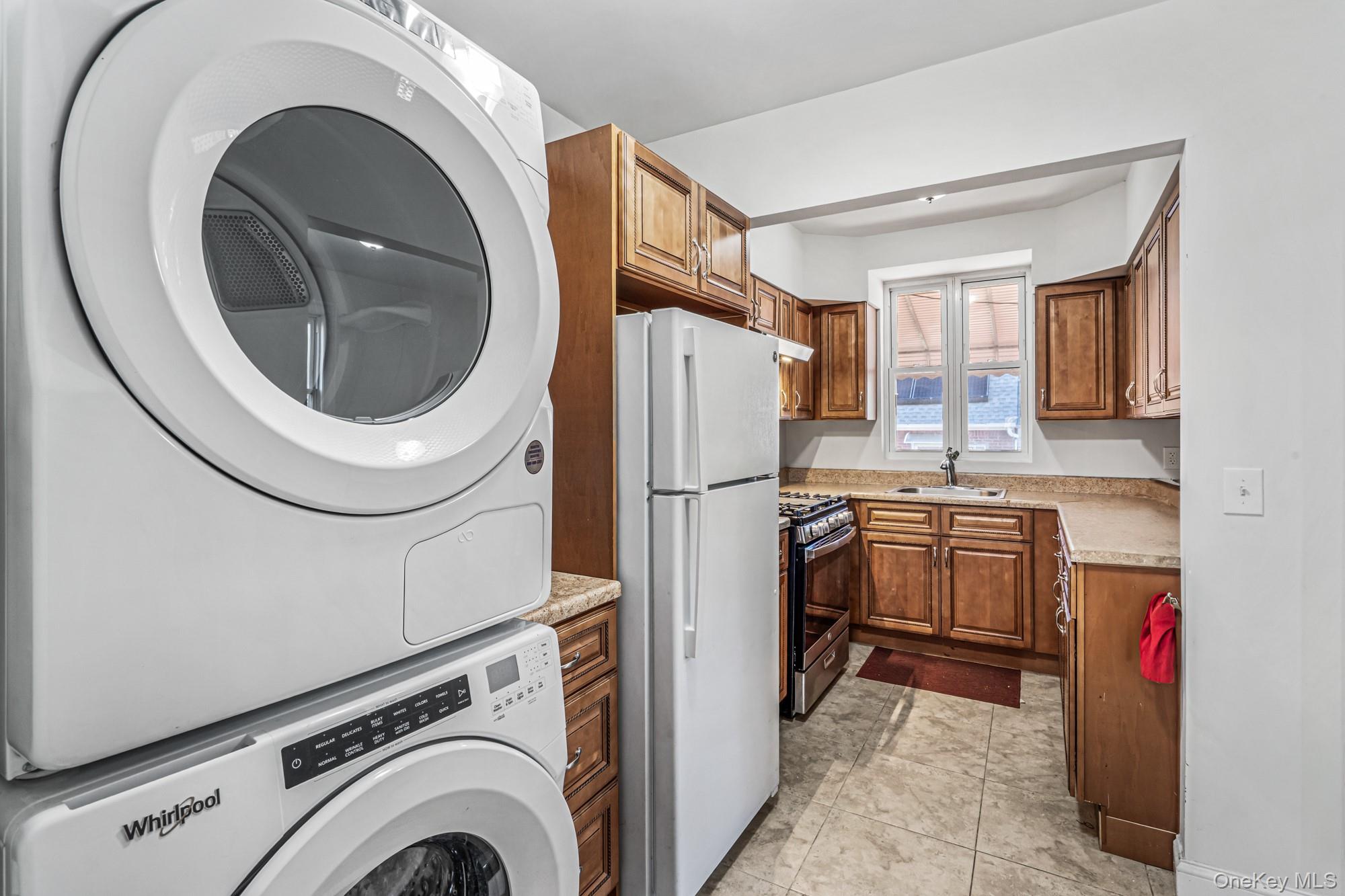 61-12 Main Street Queens, NY 11367 - Photo 18 of 35 Kitchen with freestanding refrigerator, brown cabinetry, gas range, stacked washing machine and dryer, and light tile patterned flooring