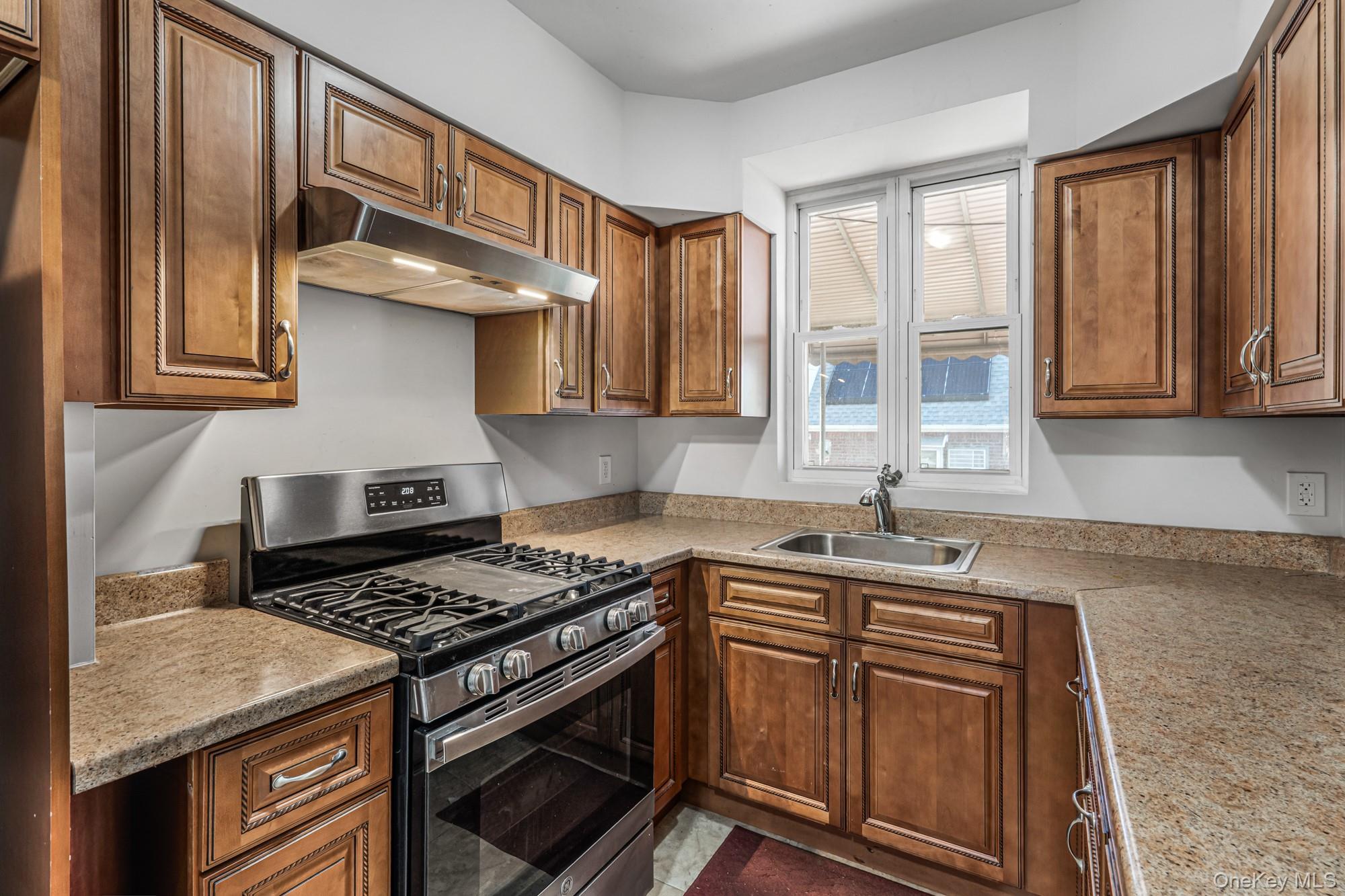 61-12 Main Street Queens, NY 11367 - Photo 19 of 35 Kitchen featuring gas stove, under cabinet range hood, brown cabinets, and light stone counters