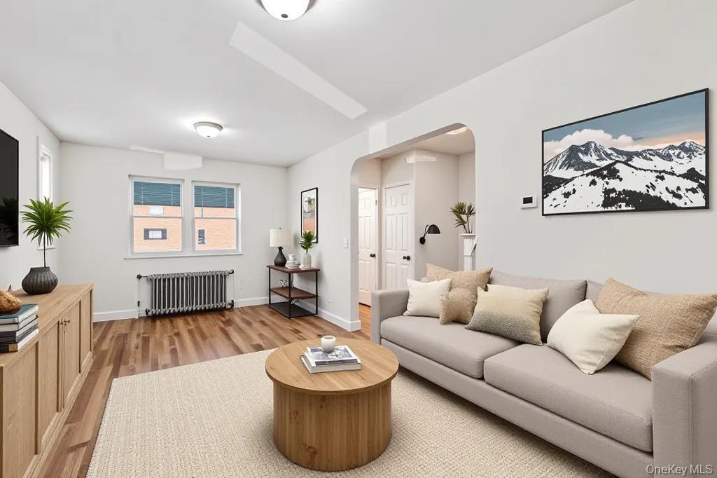 61-12 Main Street Queens, NY 11367 - Photo 2 of 35 Living room featuring arched walkways, radiator heating unit, and light wood-type flooring