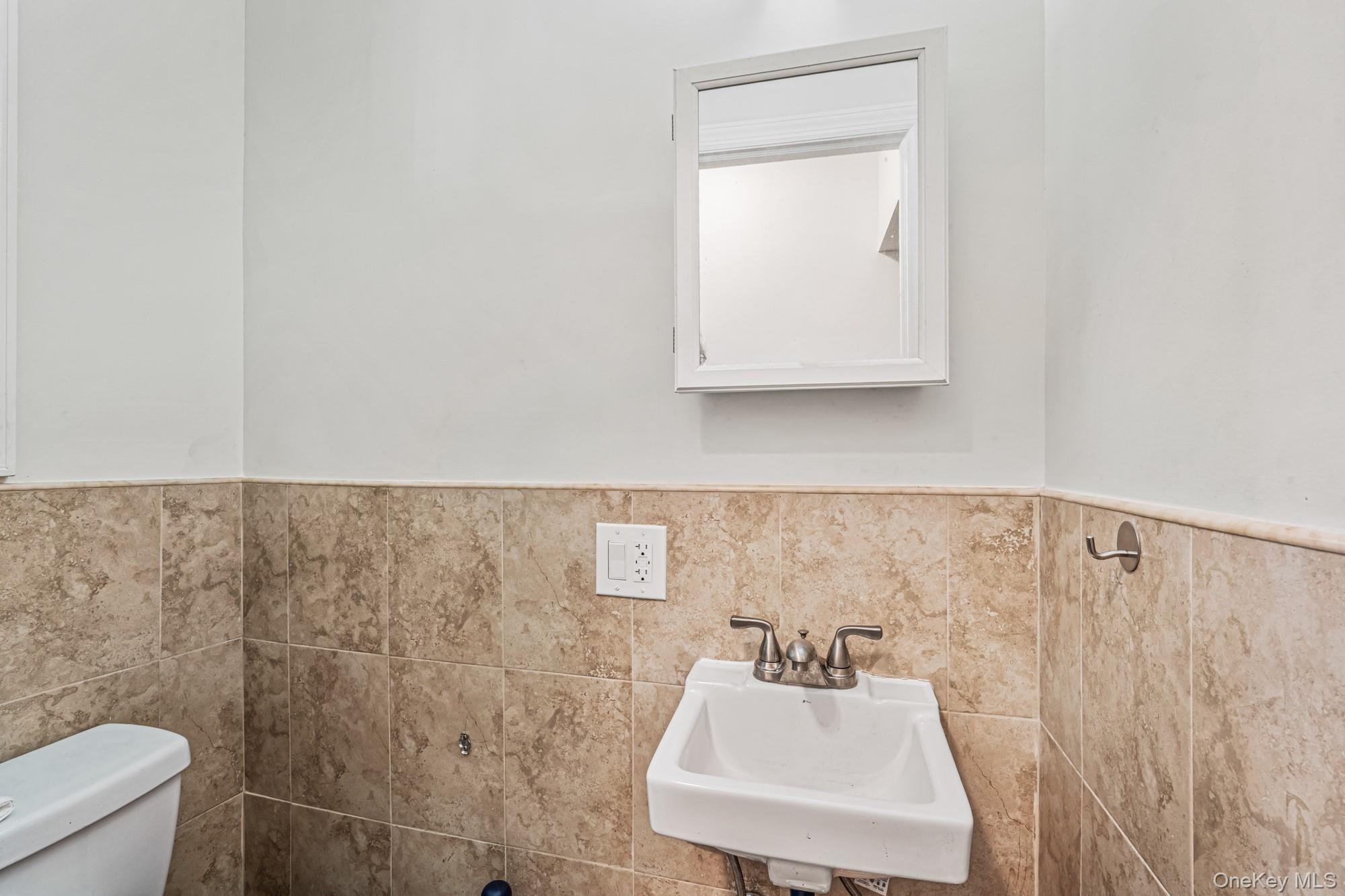 61-12 Main Street Queens, NY 11367 - Photo 21 of 35 Half bathroom featuring tile walls and a wainscoted wall