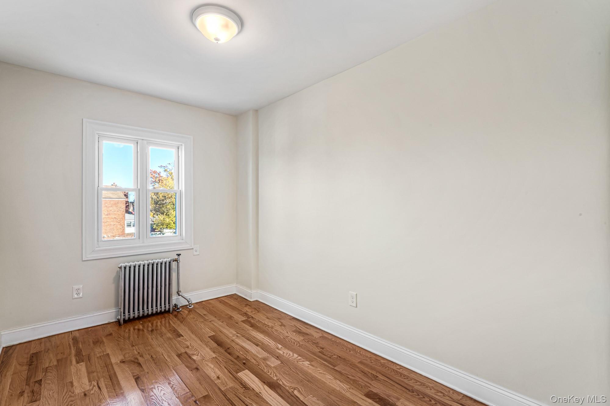 61-12 Main Street Queens, NY 11367 - Photo 27 of 35 Empty room featuring radiator and wood finished floors