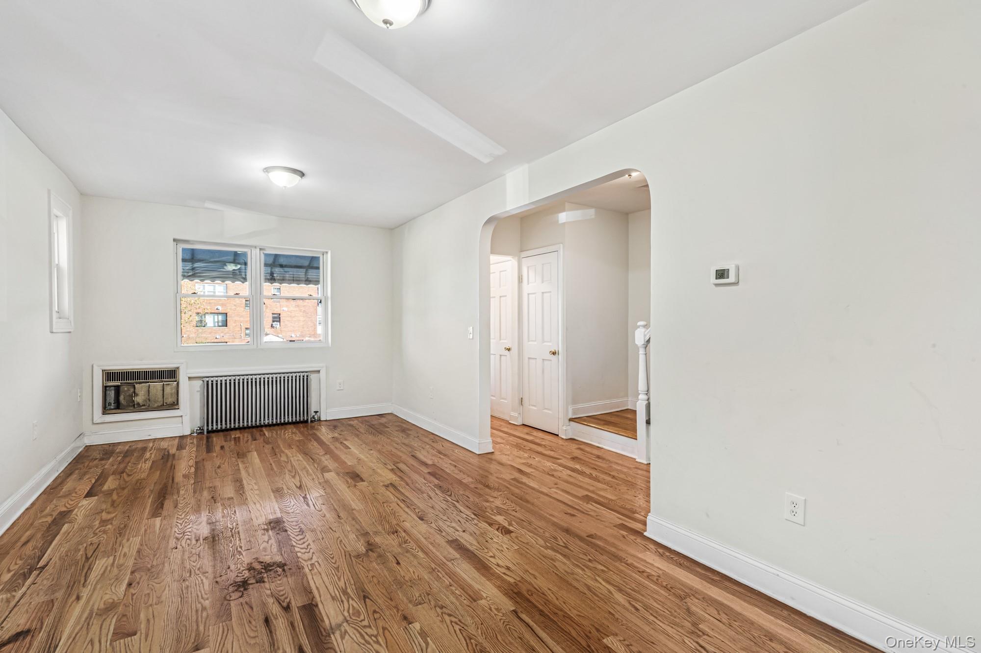 61-12 Main Street Queens, NY 11367 - Photo 3 of 35 Unfurnished living room with arched walkways, wood finished floors, radiator, and heating unit