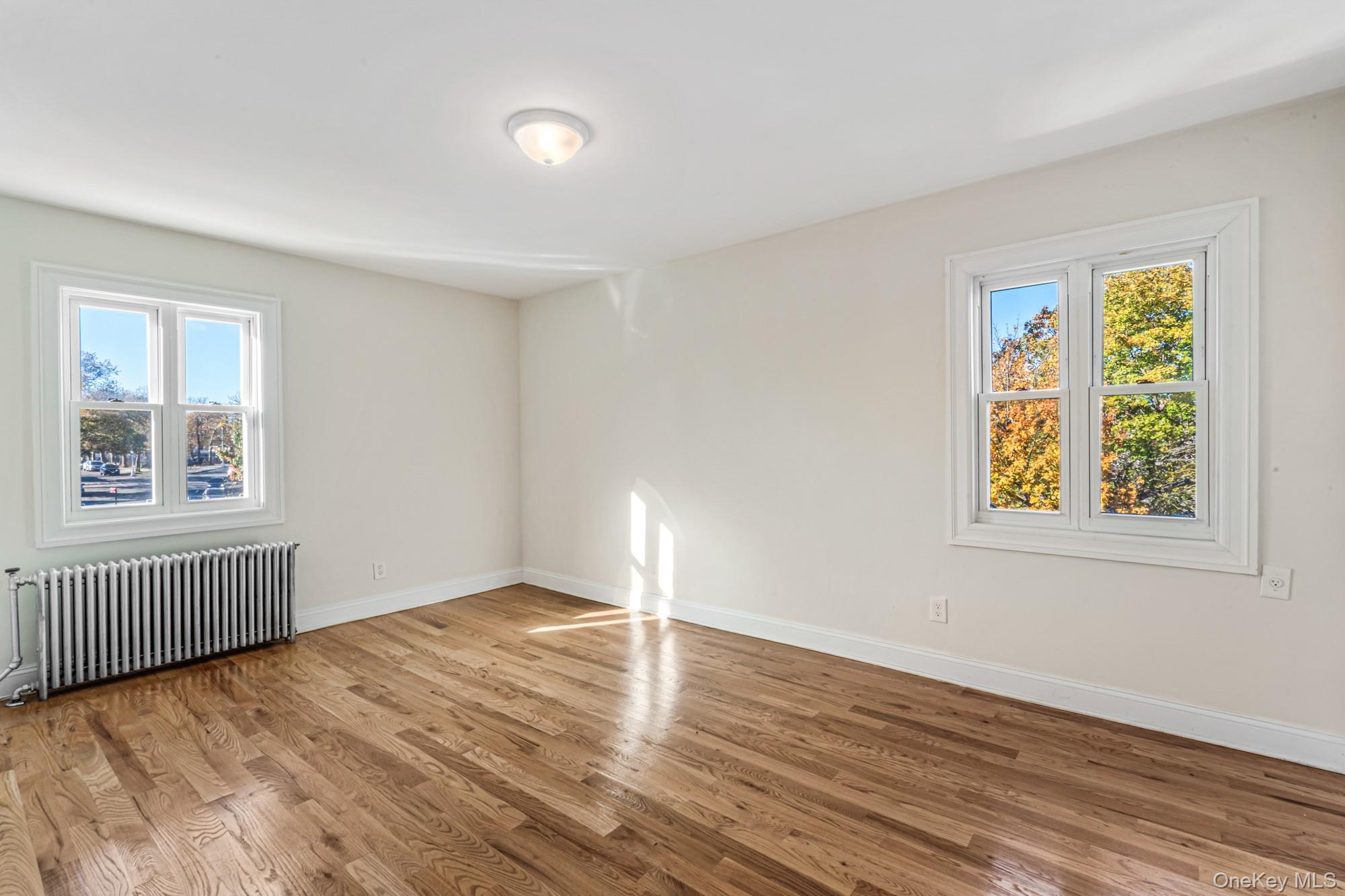 61-12 Main Street Queens, NY 11367 - Photo 9 of 35 Empty room with radiator heating unit, plenty of natural light, and light wood-type flooring