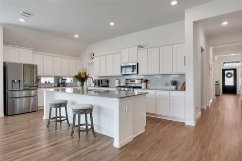 a kitchen with stainless steel appliances granite countertop a stove top oven a refrigerator a sink and white cabinets with wooden floor