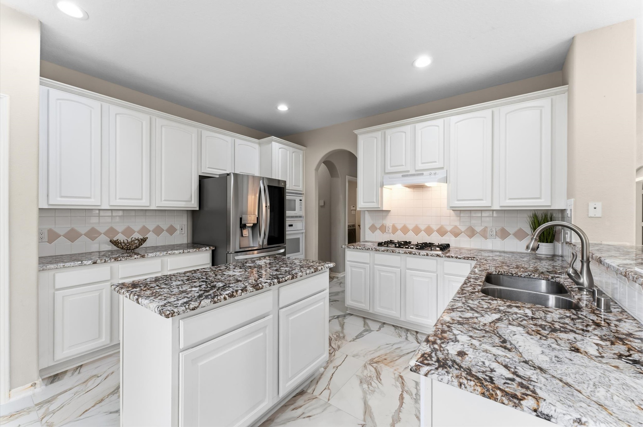 91 South Downy Willow Circle Spring, TX 77382 - Photo 16 of 50 a kitchen with kitchen island granite countertop a sink stove refrigerator and white cabinets with wooden floor