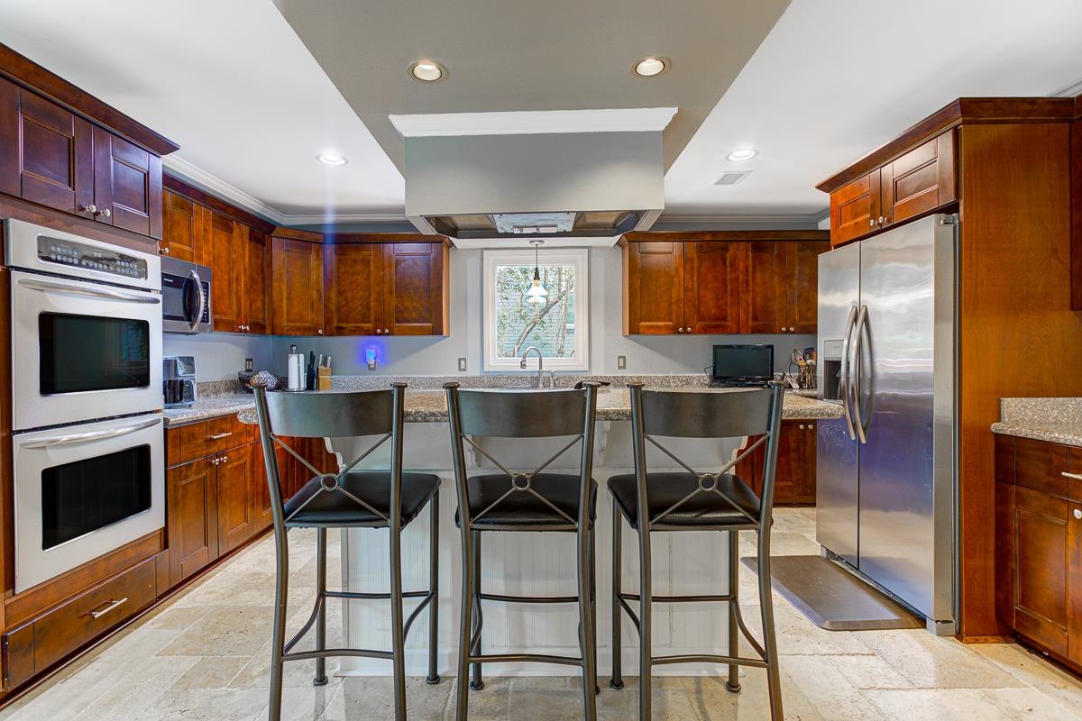 5699 Normandy Road Memphis, TN 38120 - Photo 8 of 34 Kitchen featuring an island with seating, stainless steel appliances, wood cabinetry, granite countertops, and tiled flooring