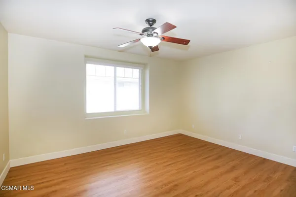 an empty room with wooden floor chandelier fan and windows