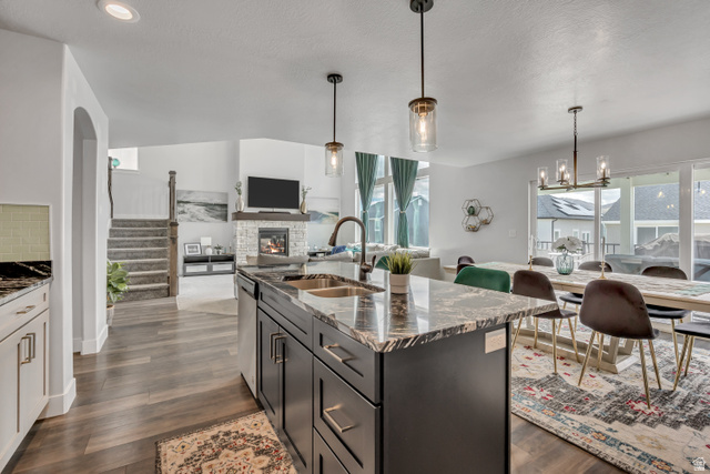 1577 Quailhill Road Saratoga Springs, UT 84045 - Photo 46 of 46 Kitchen featuring dark stone counters, open floor plan, a stone fireplace, hanging lights, and an island with sink