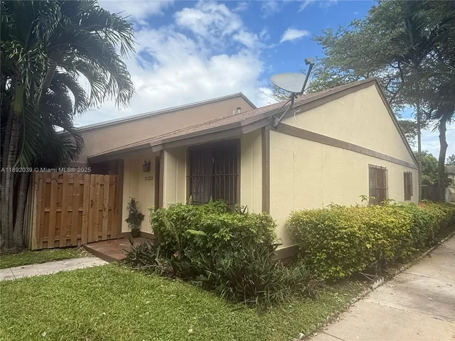 a view of a house with brick walls plants and large tree