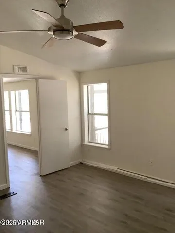 an empty room with wooden floor fan and windows