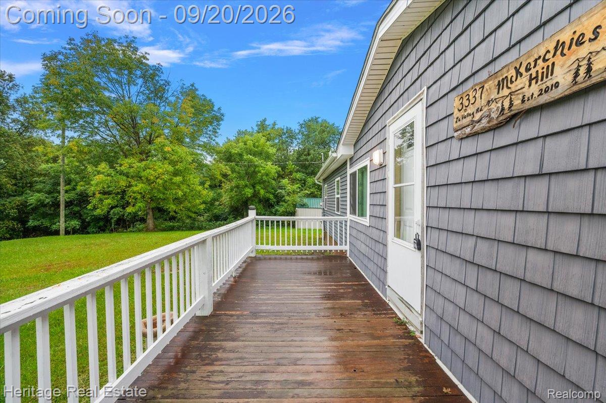 3337 Le Valley Road Columbiaville, MI 48421 - Photo 26 of 57 Expansive wood-finish deck with white railing, featuring a shingle-sided exterior with a white entry door and exterior lighting