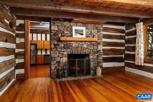 a view of an empty room with wooden floor fire place and windows