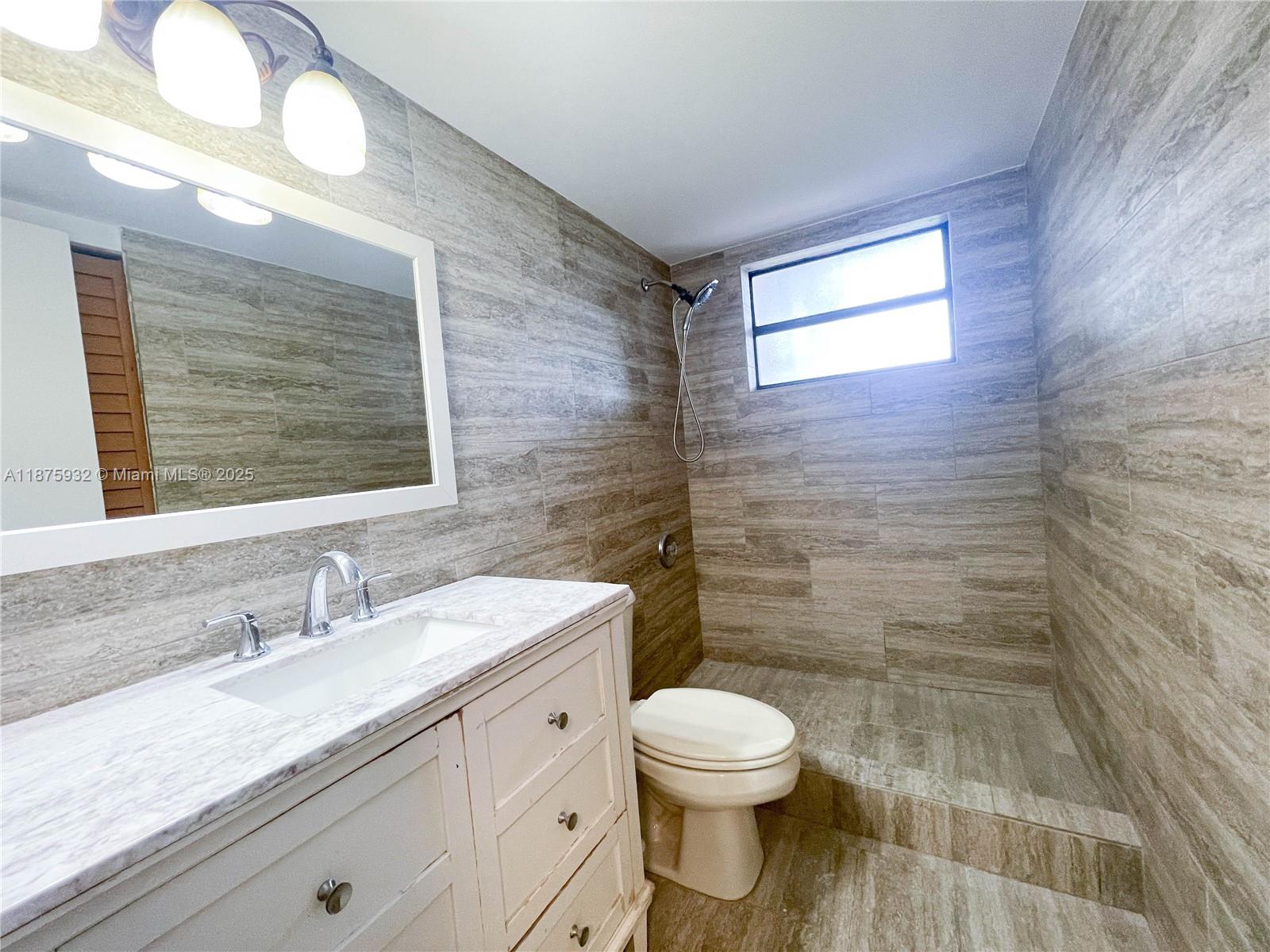 10370 Southwest 220th Street, Unit 129 Miami, FL 33190 - Photo 5 of 8 a bathroom with a granite countertop toilet a sink a mirror and a shower