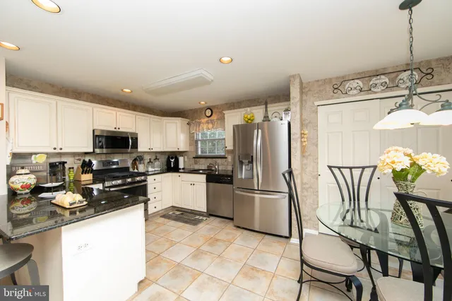 a kitchen with stainless steel appliances granite countertop a refrigerator a stove top oven a sink dishwasher and a dining table with wooden floor