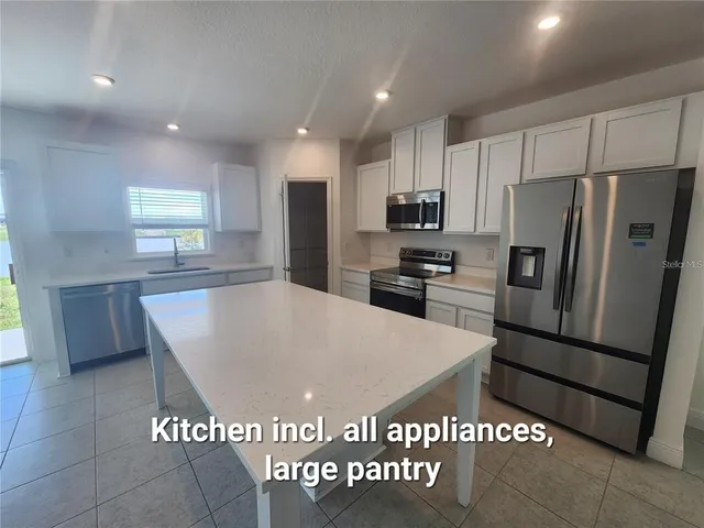 a large kitchen with kitchen island granite countertop a refrigerator a stove a sink and a refrigerator