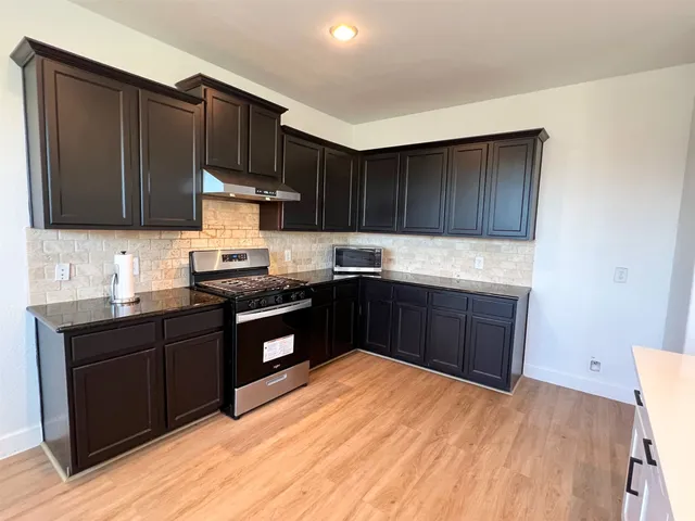 a kitchen with granite countertop a sink dishwasher a stove and black cabinets